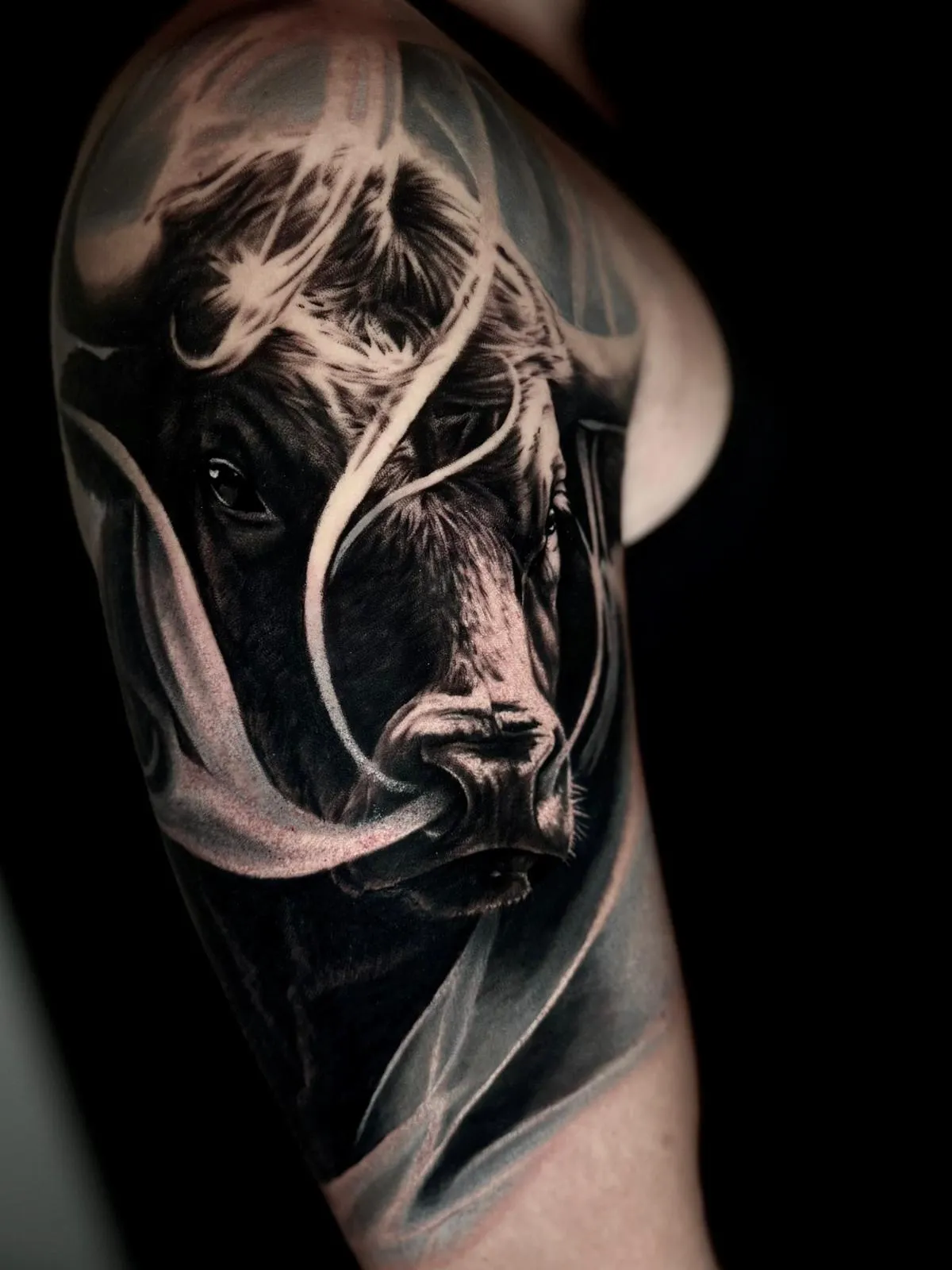 Realistic black and gray tattoo of a bull's head partially obscured by smoke on an upper arm.