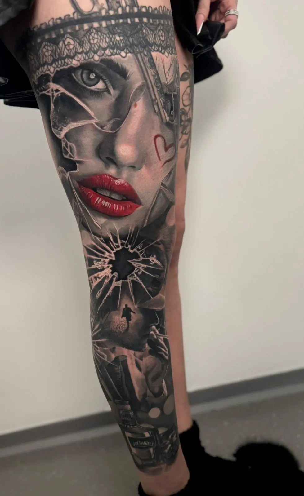 Detailed leg tattoo depicting a woman's face with red lips and shattered glass effect, a man running through broken glass, and a bottle of Jack Daniel's whiskey.