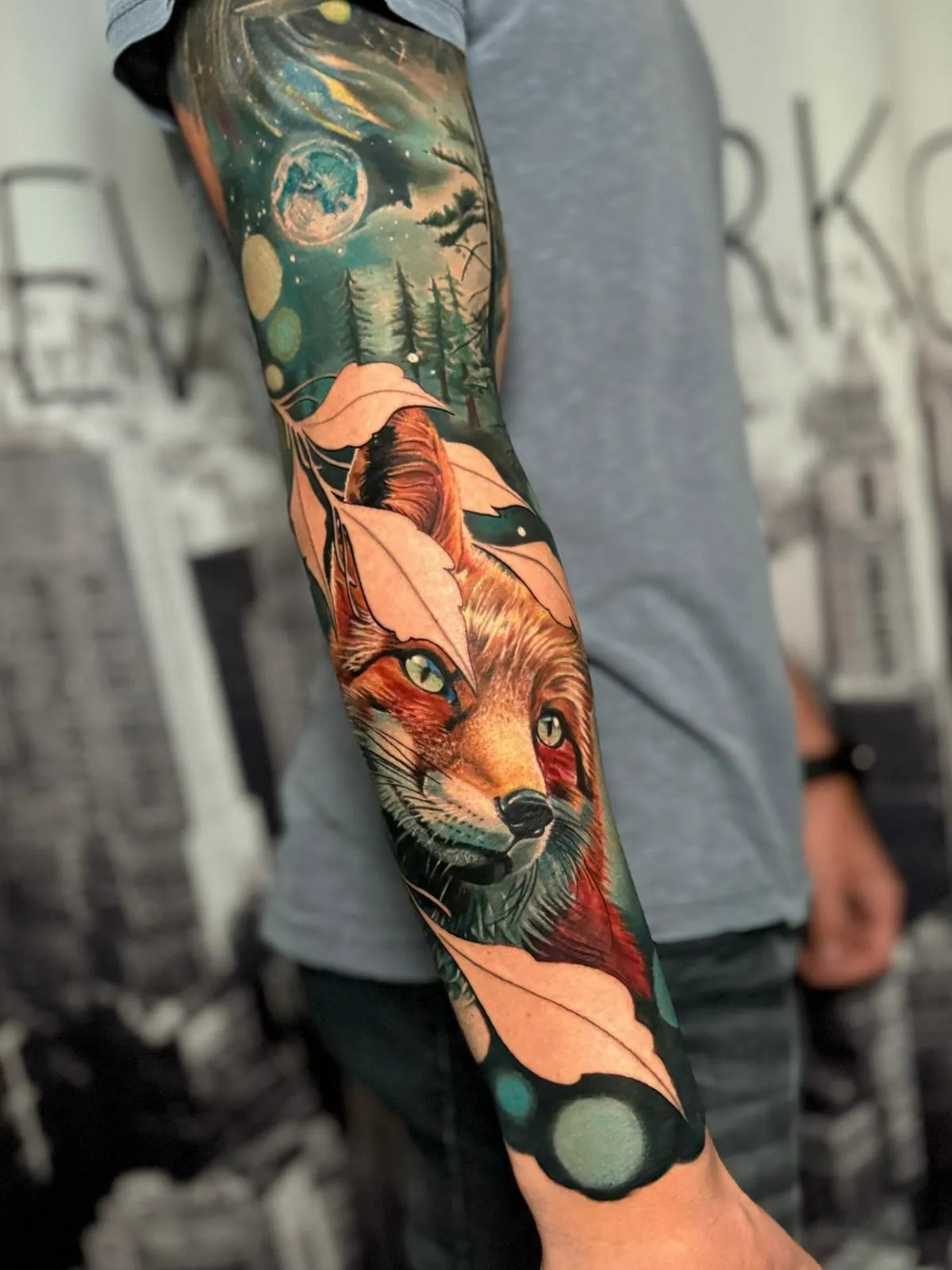 Sleeve tattoo featuring a realistic fox face surrounded by leaves, trees, and celestial elements including a full moon and stars.