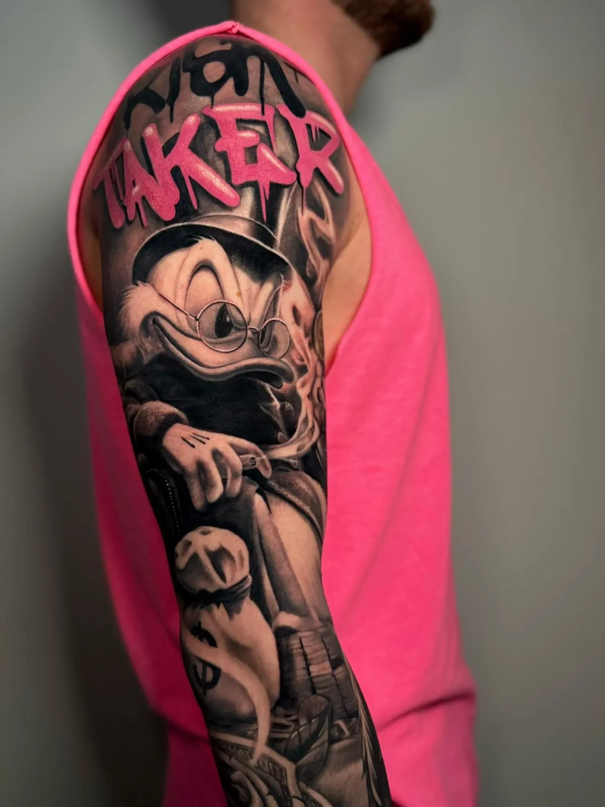 Black and grey tattoo sleeve of Scrooge McDuck wearing a hat and glasses, smoking a cigar with money bags and dollar bills, and the word 'TAKER' in pink graffiti style above.