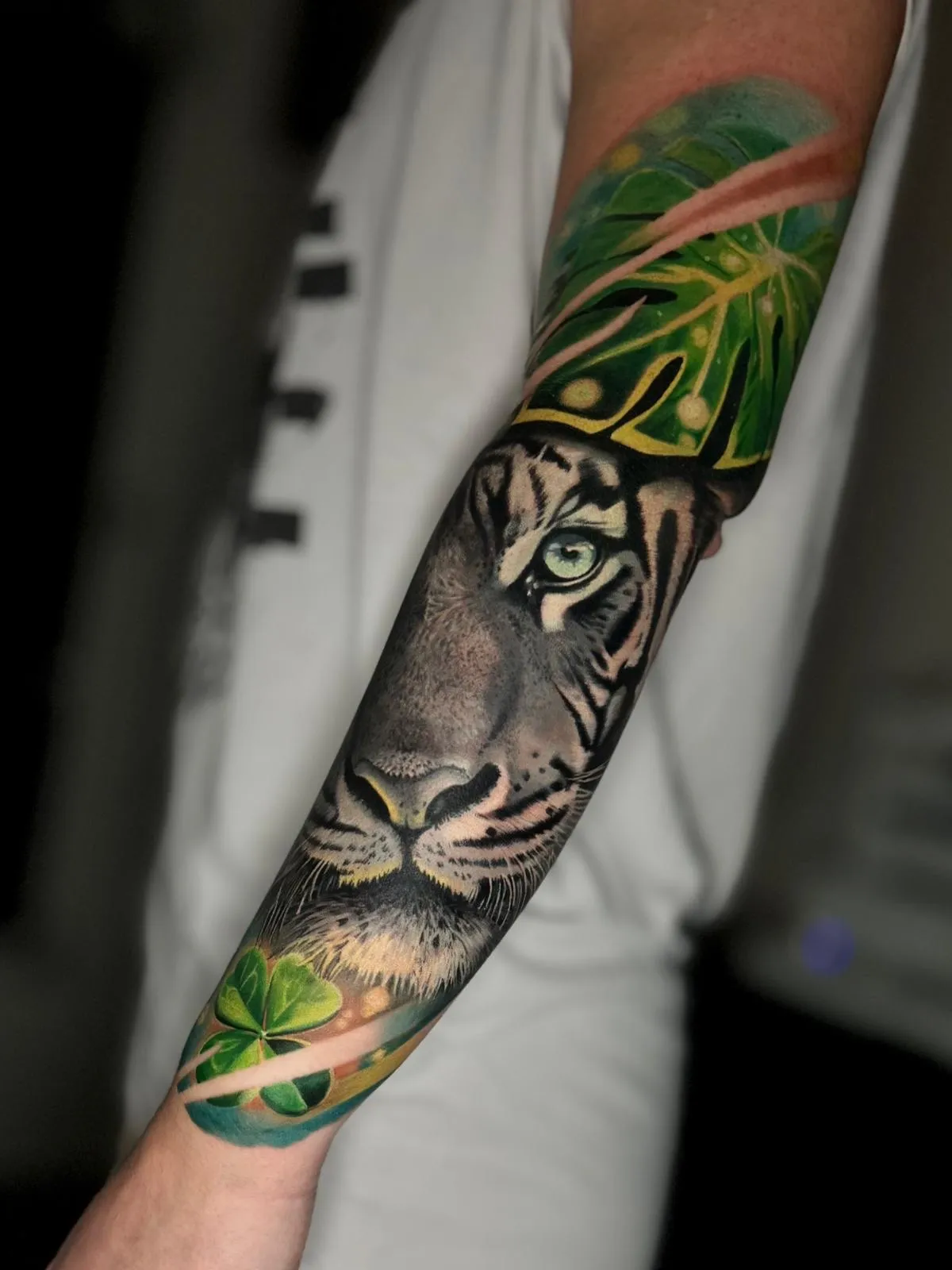 Realistic tiger face tattoo on forearm surrounded by green leaves and plants.